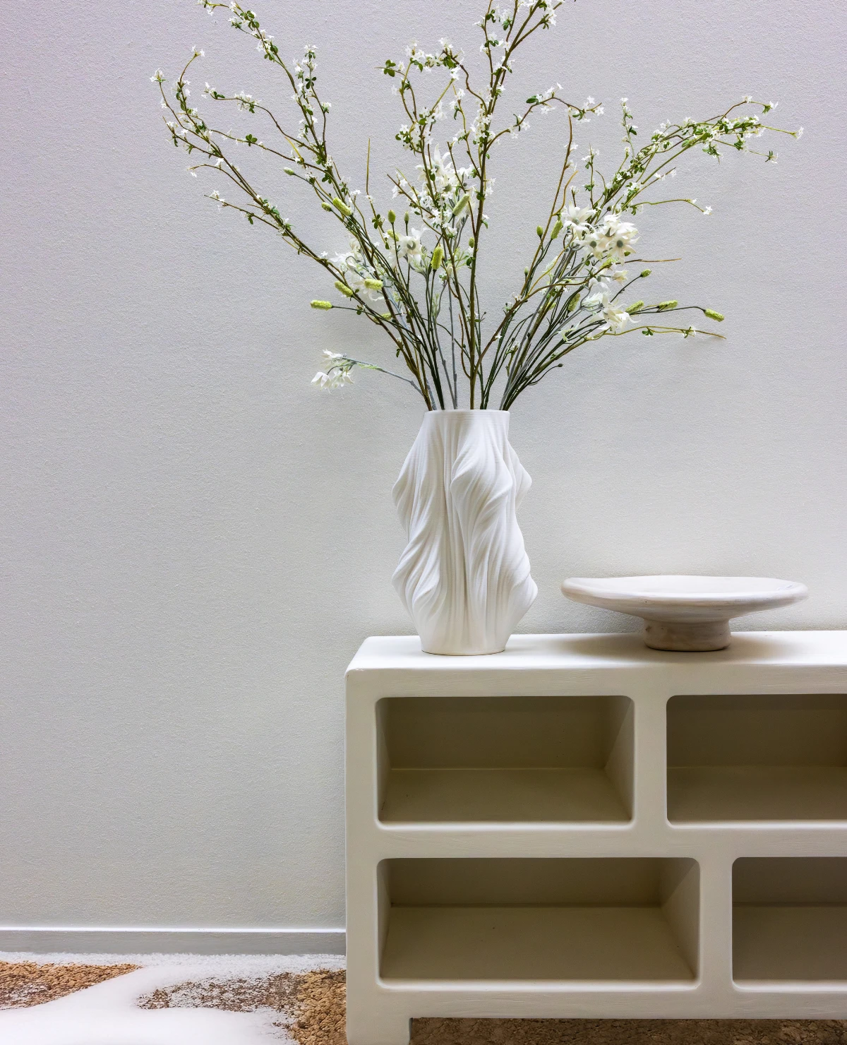 Witte designvaas met takken op een minimalistisch meubel in de trendkleuren A/W 26/27.