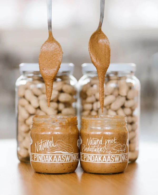 kleine potjes pindakaas met op de achtergrond twee grote potten pinda's van de pindakaaswinkel