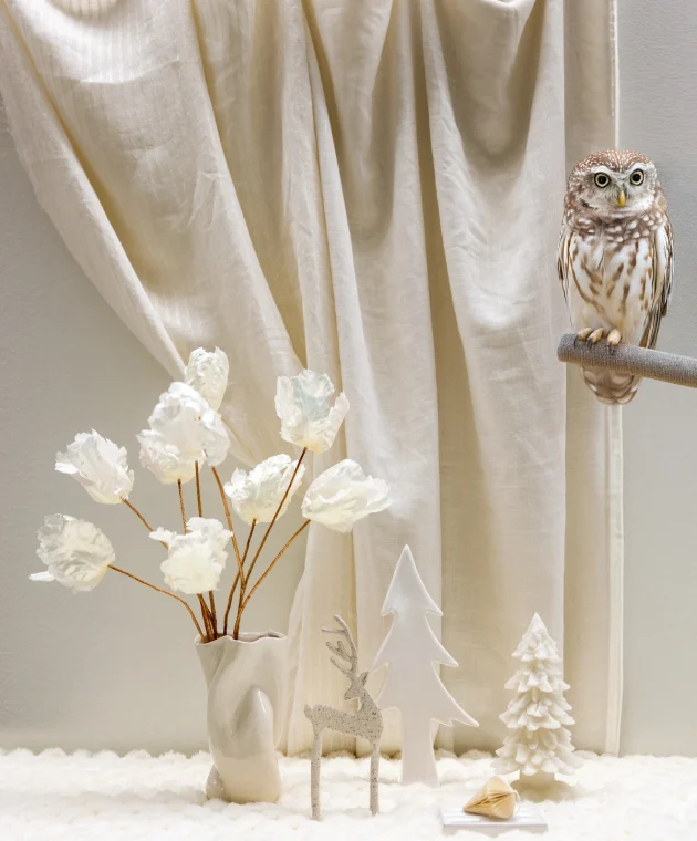 Winterse styling met witte bloemen, uildecoratie en kerstornamenten volgens de trendkleuren A/W 26/27.